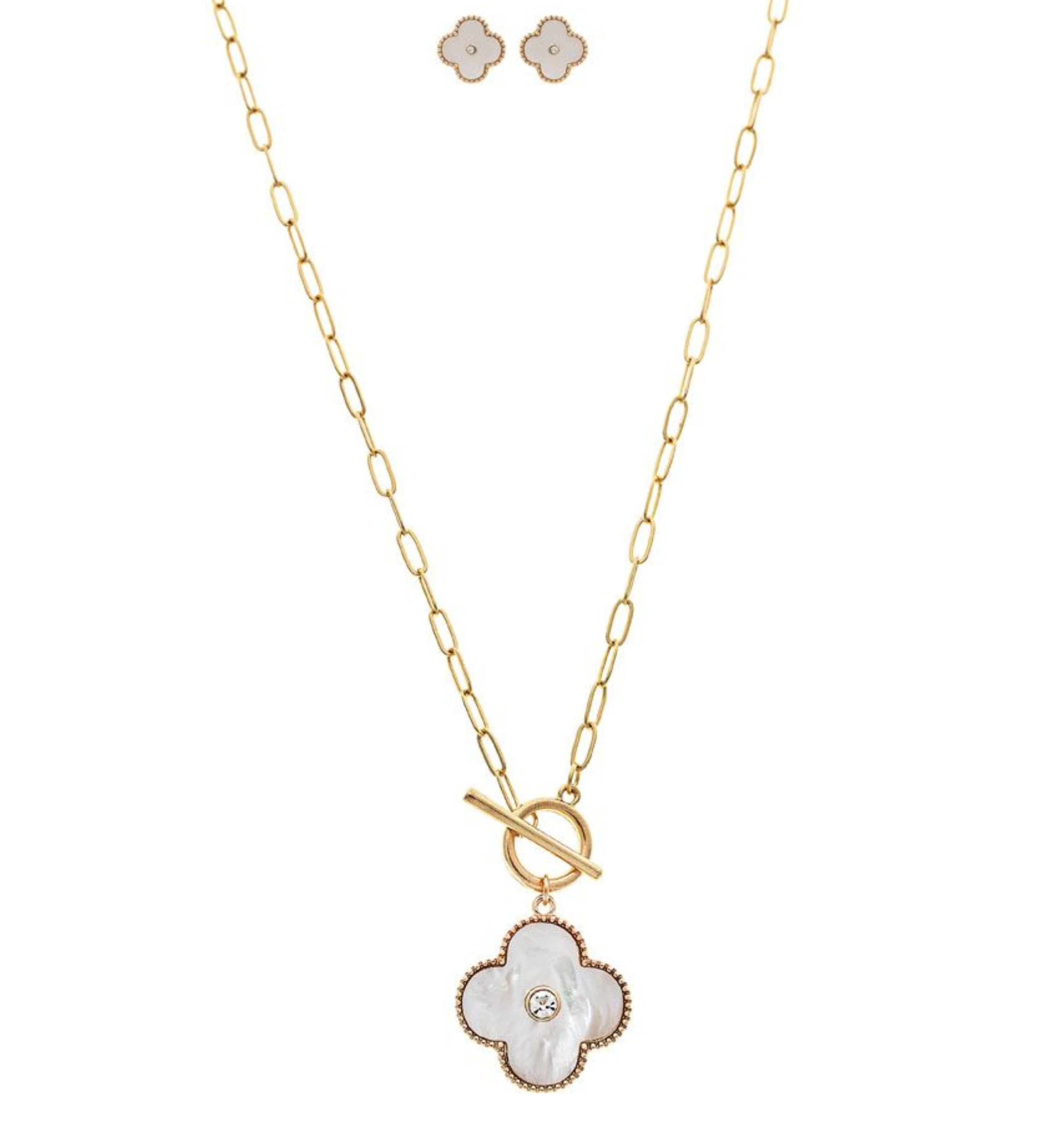 The A-Train Gold/White Shell Clover Front Toggle Necklace Set features a gold chain with a front toggle clasp, a white four-leaf clover pendant with central gem, and matching clover stud earrings.