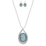The A-Train Silver Big Blue Crystal Necklace Set features a high-quality silver chain with a large blue textured oval pendant and matching blue oval drop earrings—ideal for special occasions.