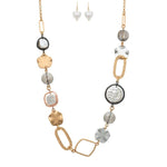 The A-Train Multi Mix Glass Faux Pearl/Metal Shape Necklace Set features a gold chain with abstract and geometric beads in gold, silver, and pearl tones, plus matching dangling heart-shaped pearl earrings on hooks.