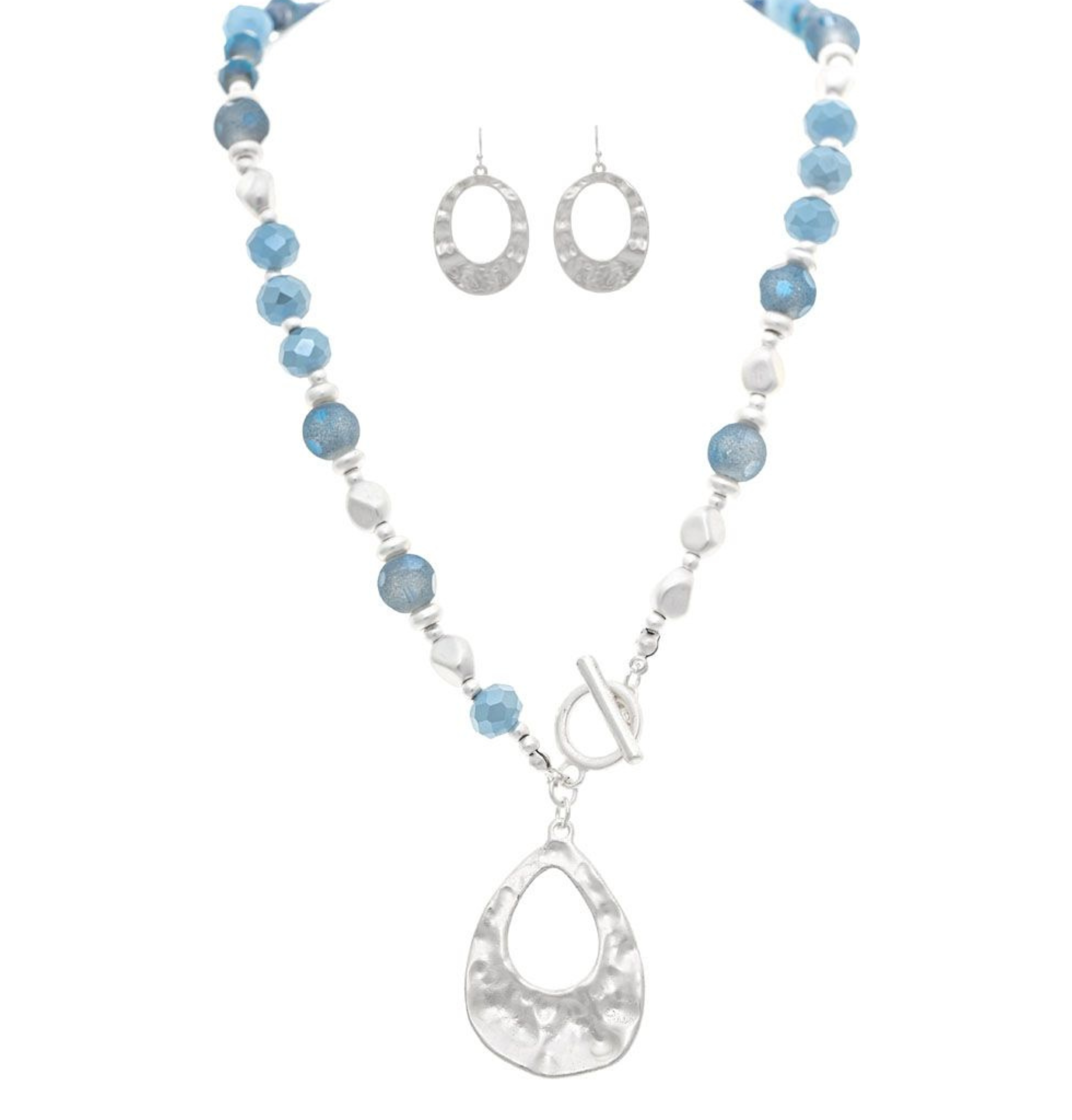 The A-Train Silver Blue Frosty Bead Teardrop Topple Necklace Set features a silver and blue beaded necklace with a large silver teardrop pendant and matching textured oval earrings, displayed on a white background.