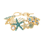 The A-Train Gold Enamel Crystal Seaside Mosaic Toggle Clasp Bracelet features sea-inspired charms—seashell, starfish, pearl, blue gemstones—set on white enamel and adorned with sparkling crystals.
