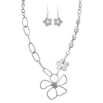 The A-Train Silver Flower Chain Link Necklace Set includes a necklace and dangle earrings with large chain links, a wire-style flower pendant, and a textured flower charm, all crafted from mixed jeweler’s metals.