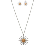 The A-Train Two-Tone Blazing Sun Necklace Set features sun-shaped pendants in mixed metals with gold-toned centers; the necklace boasts a bold sun pendant while the earrings display smaller matching designs.