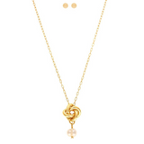 The A-Train Gold Love Knot w/ Freshwater Pearl Necklace Set features a knot pendant necklace with a freshwater pearl and matching round pearl stud earrings, elegantly displayed on a white background.