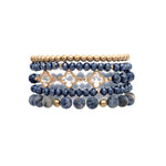 The A-Train Gold Mix Bead Sodalite Clovers 5 Pc Set Bracelet features five flexible bracelets with alternating gold and dark blue beads, including faceted blue beads and gold quatrefoil accents.