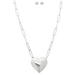 The A-Train Silver Puffy Heart Locket Chain Necklace Set features elongated links, a shiny puffed heart pendant, and matching stud earrings—displayed on a white background.