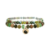 The A-Train Gold Green Color Treated Jade Bead 2 Pc Set Bracelet features two strands of multicolored beads and a gold charm with a dark stone, perfect for everyday or special occasions. Shown on a white background.