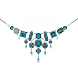 The La Dolce Vita Bib Moonlight Light Blue Necklace by Firefly features blue circular and rectangular pendants accented with dangling blue beads in an ornate, symmetrical design; this fair-trade artisan piece is a beautiful example of handmade jewelry from Guatemala.