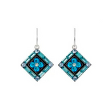 A pair of Firefly’s La Dolce Vita Diagonal Moonlight Light Blue Earrings, showcasing dangling geometric squares adorned with sparkling blue stones, silver hooks, and a central floral motif. This exquisite handmade jewelry exemplifies elegance and is thoughtfully crafted by Firefly to honor Fair Trade values.