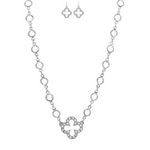The A-Train Silver Crystal By The Inch Clover Charm Necklace Set features a necklace with a cross-shaped pendant and matching earrings, both adorned with sparkling crystals and circular links for an elegant, coordinated look.