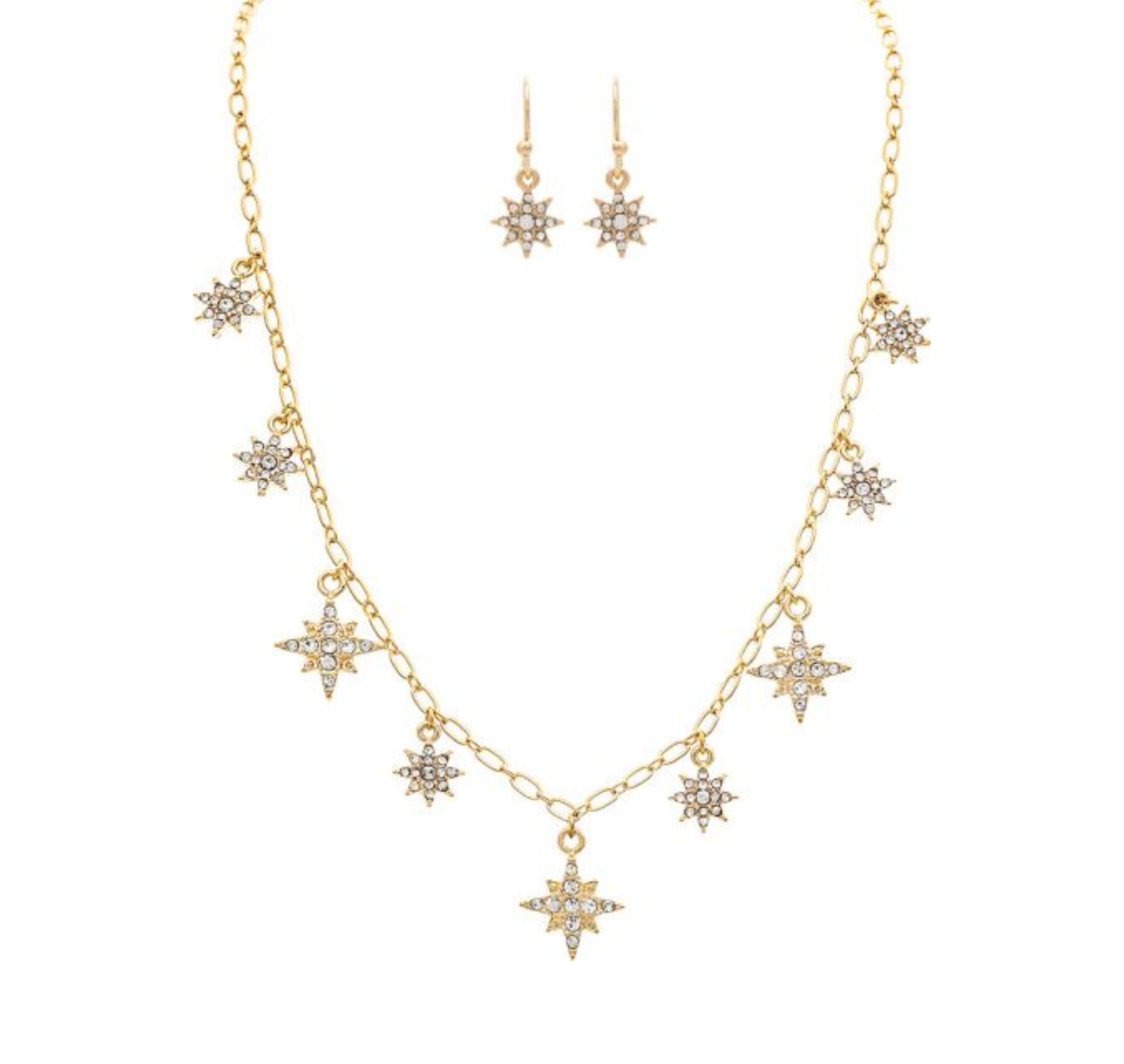 A-Trains Gold Crystal Starbursts Chain Necklace Set features a gold chain with multiple star-shaped pendants accented by clear gemstones and matching earrings, each adorned with a single sparkling star charm.
