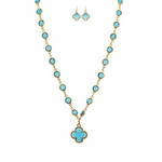 A-Trains Gold Blue Crystal By The Inch Clover Charm Necklace Set features a gold necklace with turquoise stones and a clover charm, paired with matching turquoise and gold dangle earrings, beautifully displayed on a white background.
