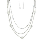 The A-Train Silver White Flowers Beads Chain Layer Necklace Set features a three-tiered necklace with delicate white beads, flower accents, and matching dangling earrings.