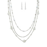 The A-Train Silver White Flowers Beads Chain Layer Necklace Set features a three-tiered necklace with delicate white beads, flower accents, and matching dangling earrings.