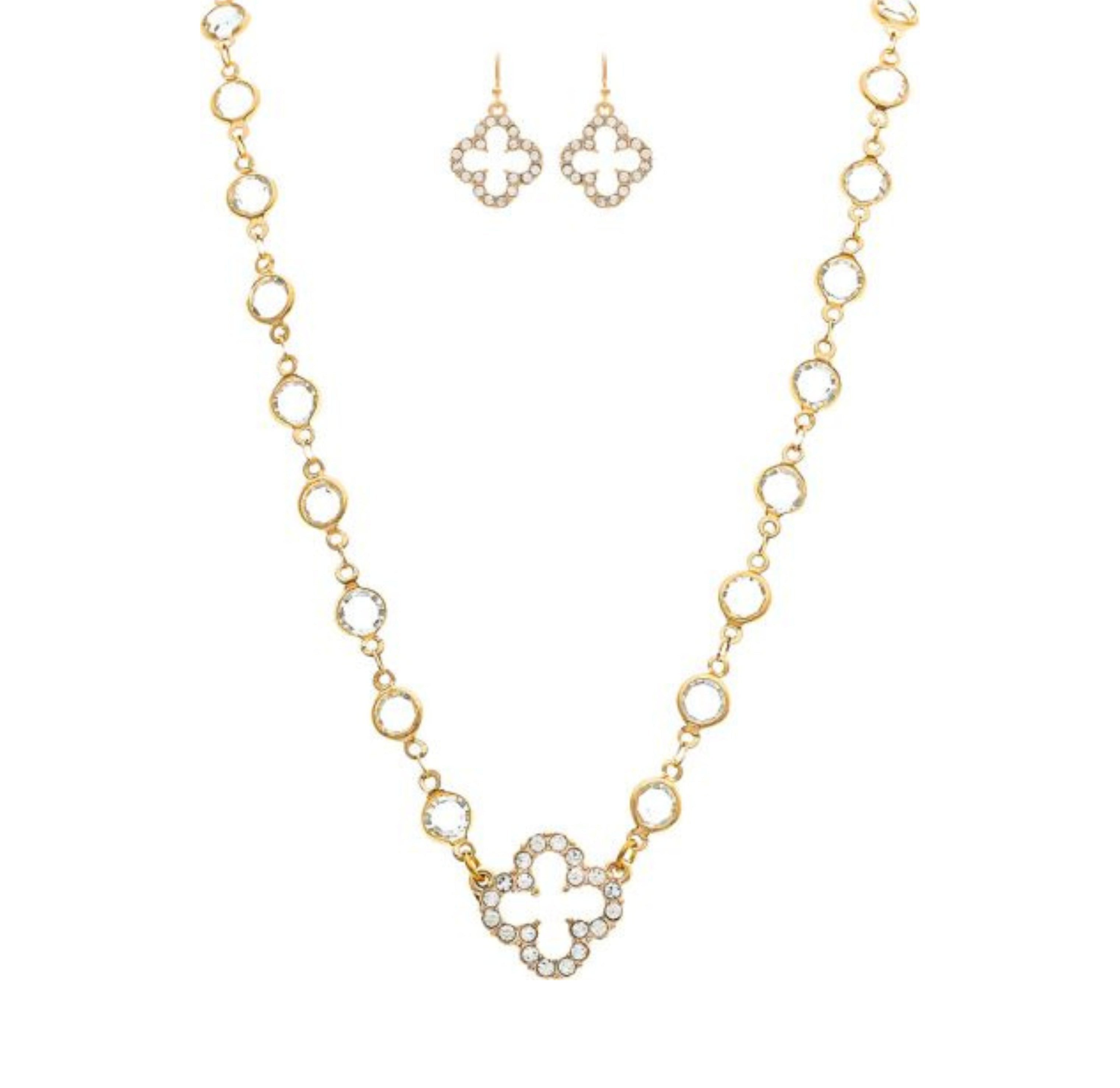 The A-Train Gold Crystal By The Inch Clover Charm Necklace Set features a necklace and earrings with linked open circles and a central gemstone-studded clover, elegantly displayed on a white background.