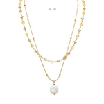 The A-Train Gold Layer Chain FWP Coin Drop Necklace Set showcases floral and geometric charms with a standout coin pearl pendant, paired with matching small round pearl stud earrings above the layered chain.