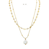 The A-Train Gold Layer Chain FWP Coin Drop Necklace Set showcases floral and geometric charms with a standout coin pearl pendant, paired with matching small round pearl stud earrings above the layered chain.