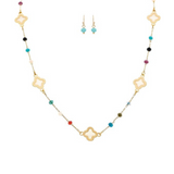The A-Train Gold Multicolor Bead & Inlay Clovers Necklace Set features a gold necklace with colorful beads and clover charms, paired with matching earrings of turquoise and gold beads, shown on a white background.