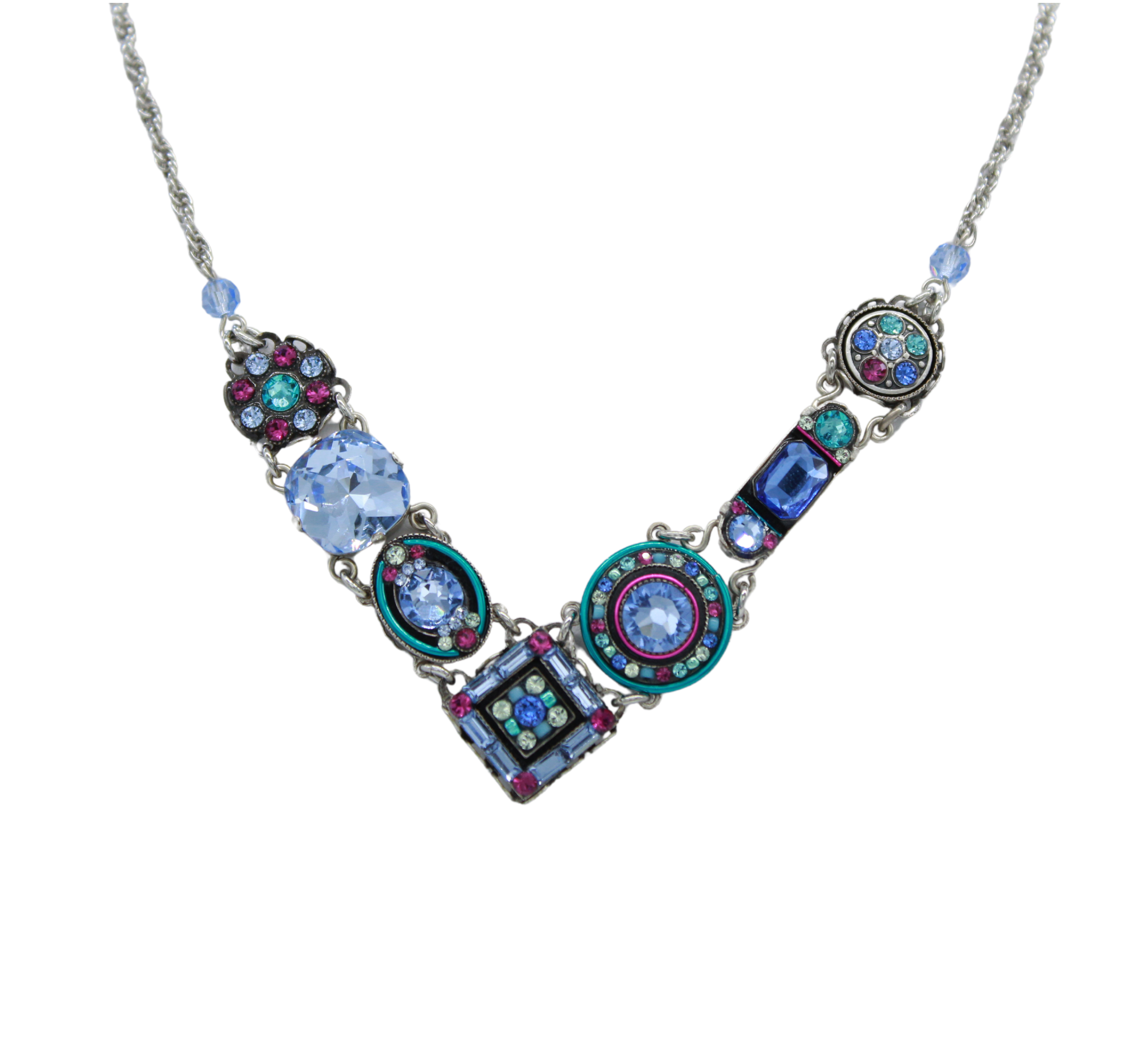 The La Dolce Vita “V” Light Blue Necklace by Firefly features a silver V-shaped pendant with blue, purple, and teal gemstones in ornate designs—a handcrafted statement piece from Guatemala.