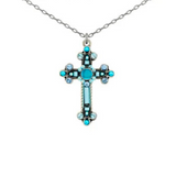 The Moonlight Large Fancy Cross Necklace by Firefly features a striking silver cross pendant adorned with turquoise and clear gemstones, suspended from a delicate chain.