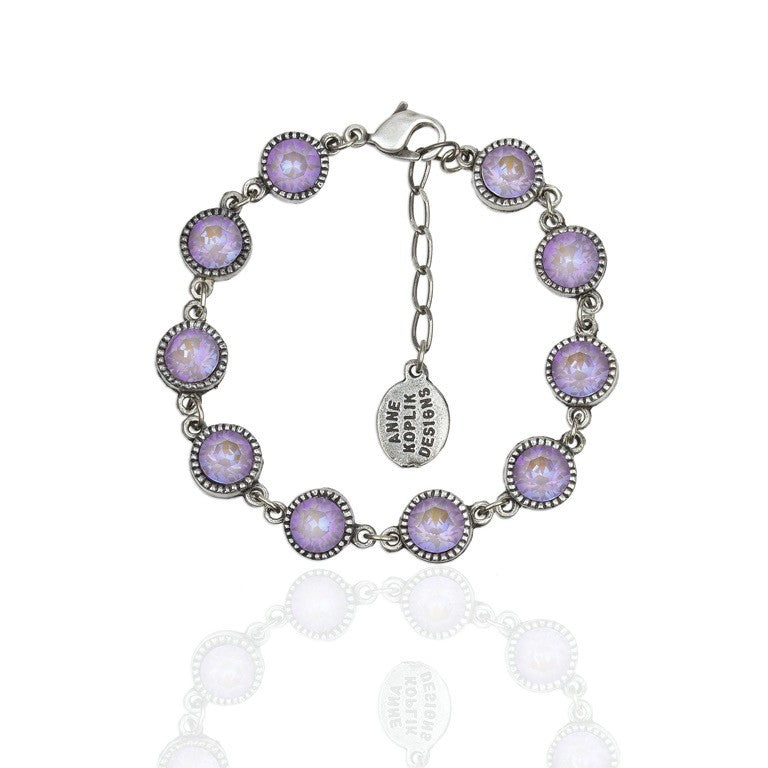 The 10 Simple Drops Lavender Bracelet by Anne Koplik Designs, Inc. features round purple gemstones in beaded settings, linked together with an adjustable chain, lobster clasp, and an oval tag engraved with the brand name.