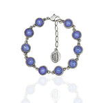 The Simple Drops Ocean Delite Bracelet by Anne Koplik Designs, Inc. features iridescent blue-purple stones in round bezels with small links, a lobster clasp, and an oval tag etched with the brand name.