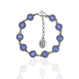 The Simple Drops Ocean Delite Bracelet by Anne Koplik Designs, Inc. features iridescent blue-purple stones in round bezels with small links, a lobster clasp, and an oval tag etched with the brand name.