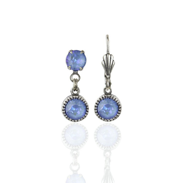 Simple Drop Ocean Delite Earrings by Anne Koplik Designs, Inc. feature silver-toned drops with two round blue gemstones on each earring—one small above a larger dangle. Lead free, these earrings add elegance to any look and are shown against a white background.