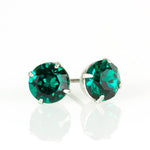 The Simple Post Emerald Earrings by Anne Koplik Designs, Inc. feature round emerald crystals in silver prongs, handcrafted for brilliant shine on a reflective white surface.