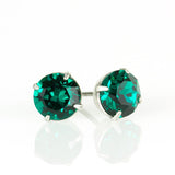 The Simple Post Emerald Earrings by Anne Koplik Designs, Inc. feature round emerald crystals in silver prongs, handcrafted for brilliant shine on a reflective white surface.