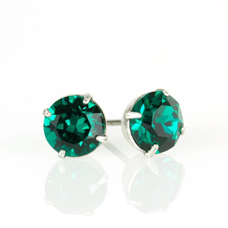 The Simple Post Emerald Earrings by Anne Koplik Designs, Inc. feature round emerald crystals in silver prongs, handcrafted for brilliant shine on a reflective white surface.