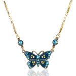 The Enamel & Stone Teal Butterfly Necklace by Anne Koplik Designs, Inc. features a butterfly pendant with blue and yellow stones and two round blue crystals on a decorative gold chain—a refined crystal-embellished accessory.