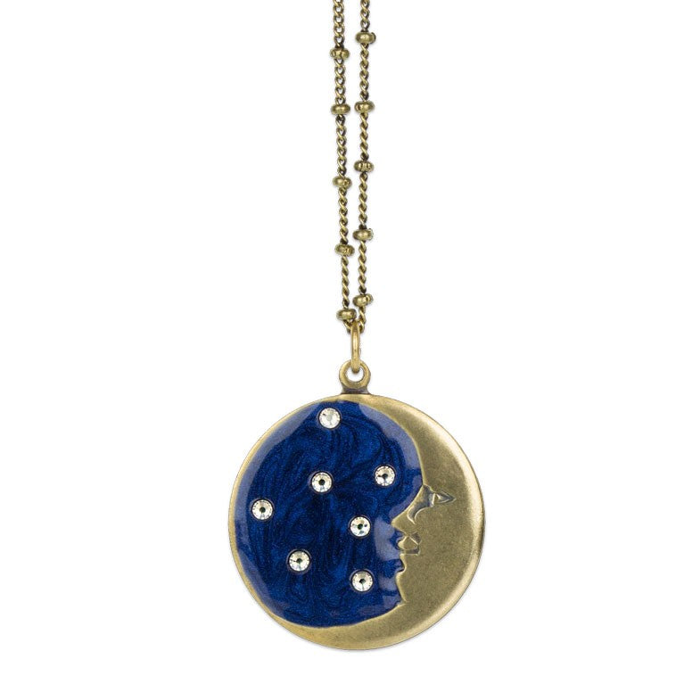The 1/2 Moon Face/Stars Necklace by Anne Koplik Designs, Inc. is a gold enameled piece with a circular charm featuring a cutout face profile, deep blue fill, and sparkling star-like crystals.