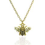 The Whimsy Flying Bee Necklace by Anne Koplik Designs, Inc. features a gold chain with a detailed bee pendant accented by black and gold stripes and crystal-adorned wings—an elegant addition to any jewelry collection.