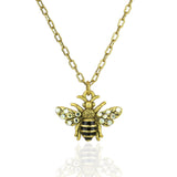 The Whimsy Flying Bee Necklace by Anne Koplik Designs, Inc. features a gold chain with a detailed bee pendant accented by black and gold stripes and crystal-adorned wings—an elegant addition to any jewelry collection.
