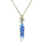 The Enamel And Stone Blue Jay Feather Necklace by Anne Koplik Designs, Inc. features a gold beaded chain, blue feather pendant with hand-painted metallic edges, a blue feather charm, white pearl, and clear crystal for added elegance.