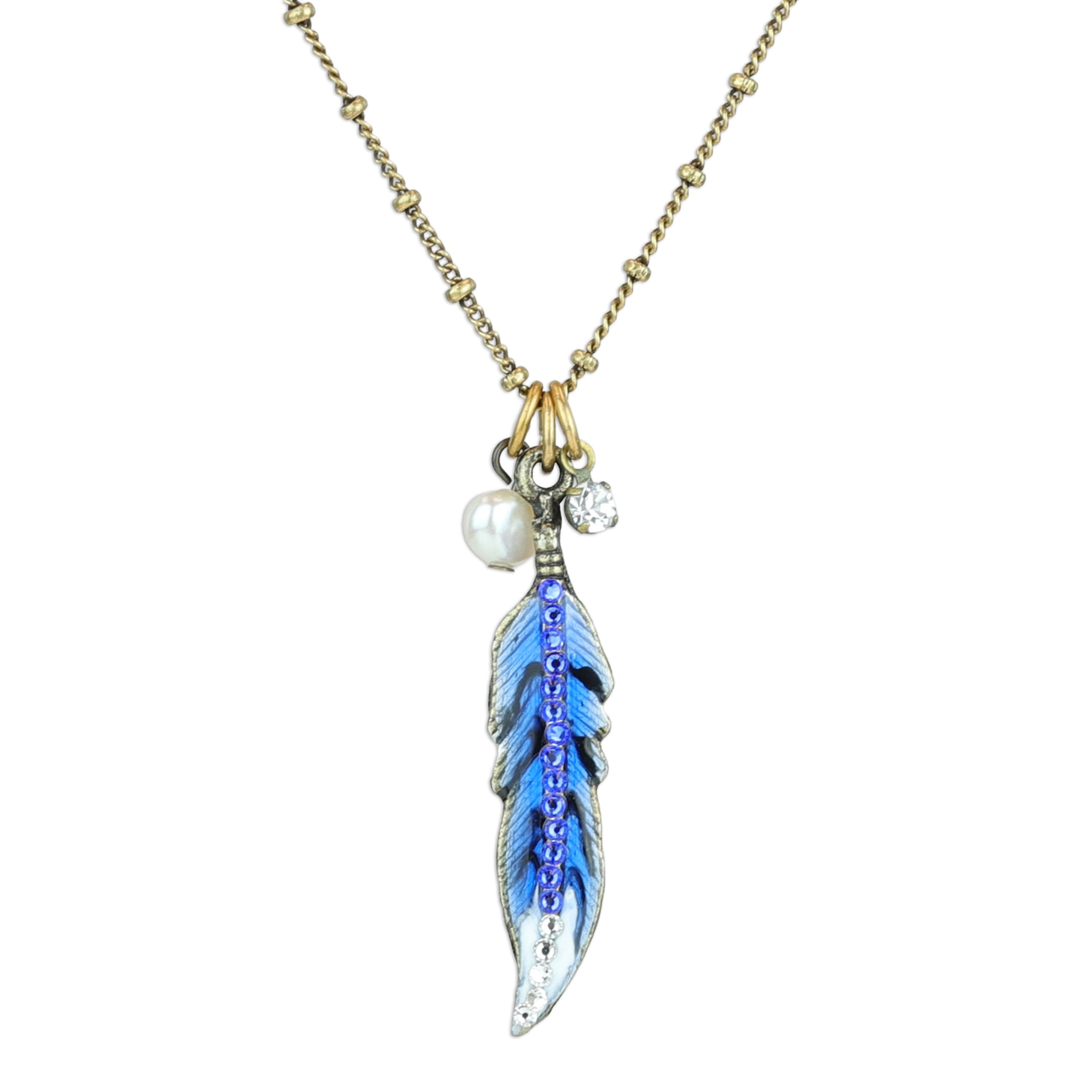 The Enamel And Stone Blue Jay Feather Necklace by Anne Koplik Designs, Inc. features a gold beaded chain, blue feather pendant with hand-painted metallic edges, a blue feather charm, white pearl, and clear crystal for added elegance.