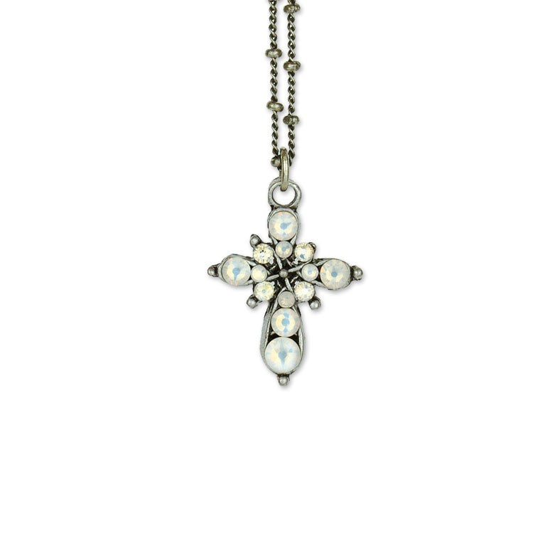 The Small Stone Fancy Cross White Opal Necklace by Anne Koplik Designs, Inc. features a vintage-inspired cross pendant with round white opal stones and sparkling crystals in a floral pattern on a silver chain, displayed against a white background.