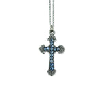 The Anne Koplik Designs, Inc. Mini Blue Crystal Pave Cross Necklace features a silver-plated cross pendant with blue crystals and decorative edges, suspended from a silver chain on a white background.