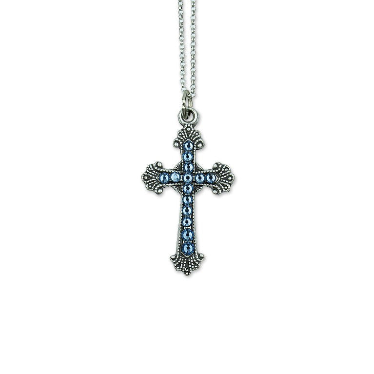 The Anne Koplik Designs, Inc. Mini Blue Crystal Pave Cross Necklace features a silver-plated cross pendant with blue crystals and decorative edges, suspended from a silver chain on a white background.