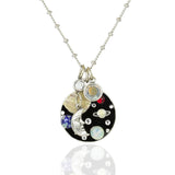 The Jumble of Planets and Moon Necklace by Anne Koplik Designs, Inc. features a circular pendant with a Man in the Moon charm, colorful planet accents, and crystals—a miniature solar system on a silver chain.
